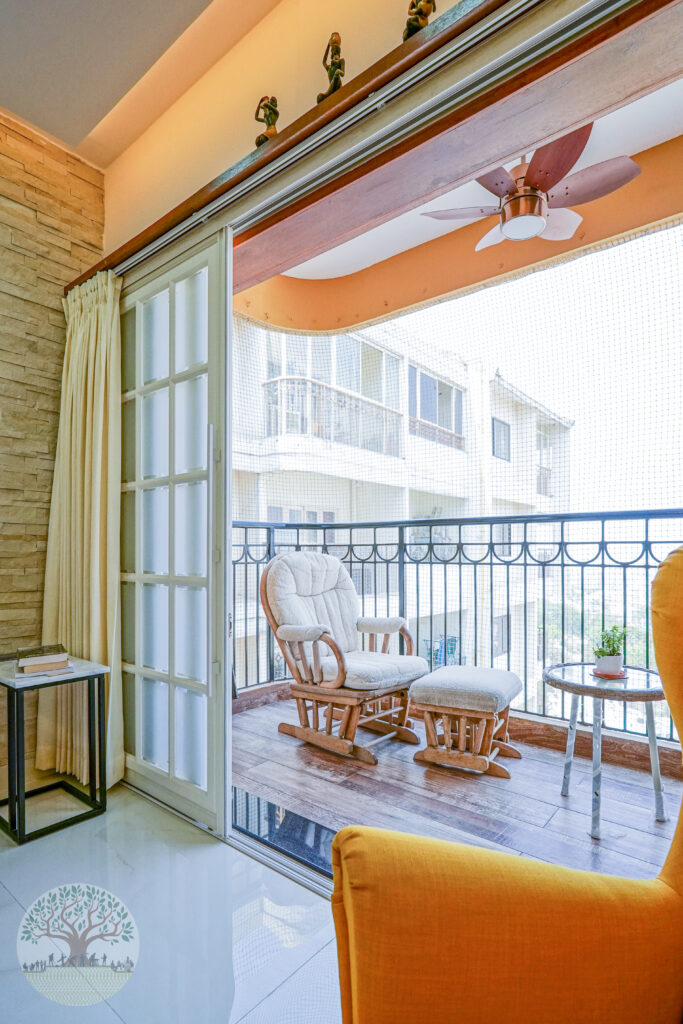 A balcony with a wooden rocking chair and ottoman, accessed through sliding glass doors, next to a textured interior wall.