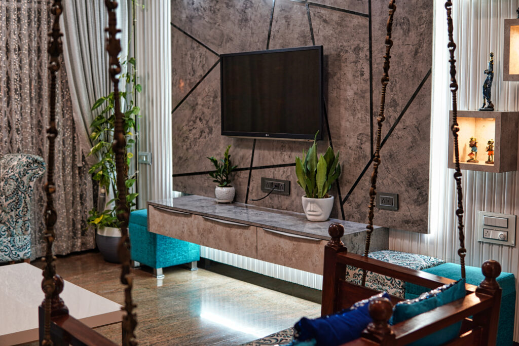Modern TV unit mounted on a textured geometric accent wall, flanked by indoor plants and turquoise seating.