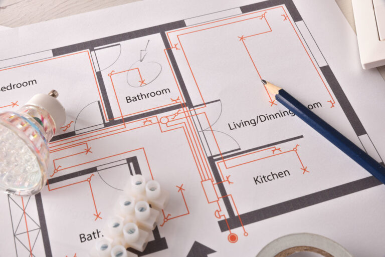 Close-up of a house floor plan with electrical wiring marked in orange, next to a pencil and electrical components.