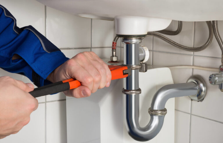 Plumber using a wrench to tighten the pipe beneath a sink.